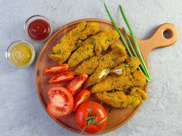 fried chicken fingers and tomatoes on a wooden platter from Buddig