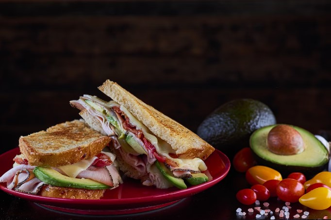 Ham sandwich with cheese and avocado on a red plate